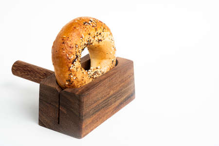 A single freshly baked bagel propped on a wood slicing stand set on a plain white background.の写真素材