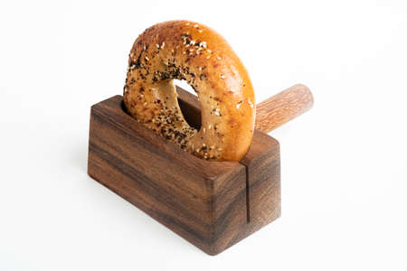 A single freshly baked bagel propped on a wood slicing stand set on a plain white background.の写真素材