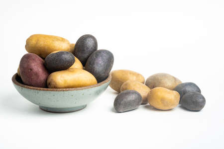 An assorted color raw and fresh potatoes artfully arranged on bowl and table set on plain white background.の写真素材