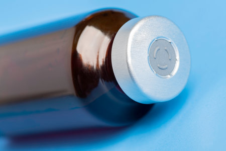 A macro shot with selective focus of an amber color vaccine injection bottle set on a plain blue background.の写真素材