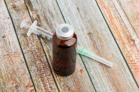 A close-up shot of an hygienic single-use plastic disposable syringe injection with amber color vial set on wood background.の写真素材