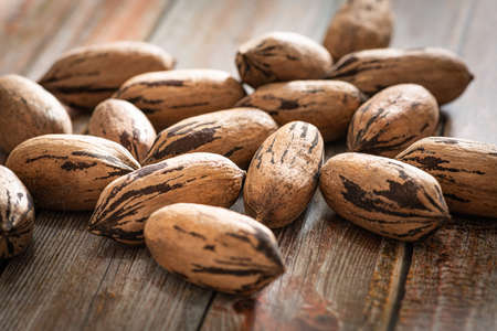 A macro shot with selective focus of a handful of pecan nuts in shells set on a wood table.