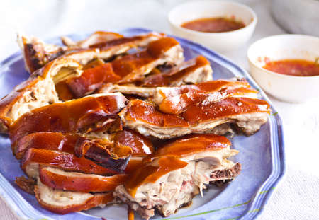 Roast pork decorated with some onions, rosemary and some colorful peppercorns on a yellow plateの写真素材