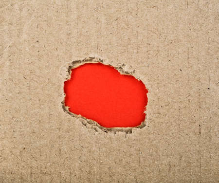 Ripped hole with red paper in cardboardの写真素材