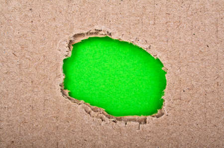 Ripped hole with green paper in cardboardの写真素材