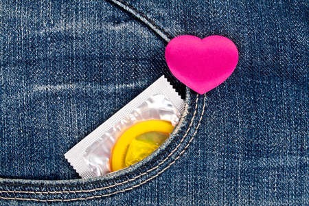 Violet heart and yellow condom in blue jeans pocket