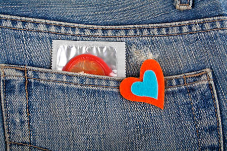 Red condom in blue jeans pocket and colored heartの写真素材