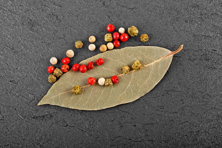 Dried bay laurel leaf and peppercorns on black background
