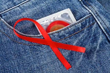 Red condom in blue jeans pocket and Aids awareness red ribbonの写真素材