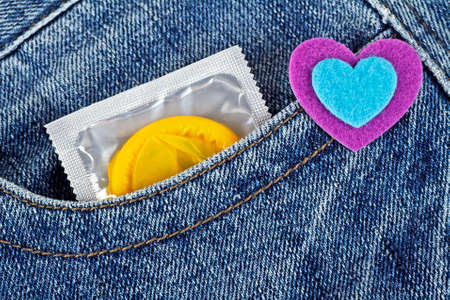 Yellow condom in blue jeans pocket and colored heartの写真素材