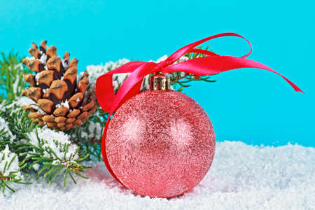 Branch of Christmas tree, pine cone and Christmas ball in snow on blue backgroundの写真素材