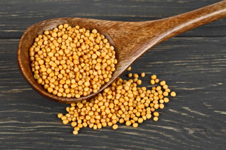 Mustard seeds on wooden spoon against wooden backgroundの写真素材