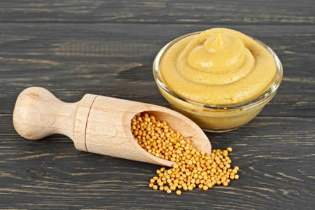 Mustard seeds and sauce in glass bowl on wooden background