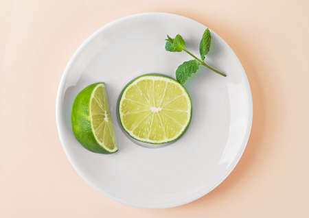 Fresh lime with mint leaves on white plate. Beige background.の写真素材