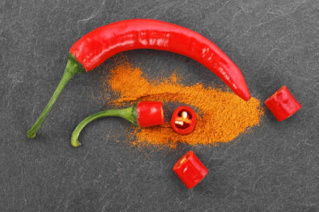 Red chili pepper slices and powder on black stone table