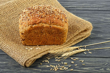 Black bread with spikelets and grain on a wooden table
