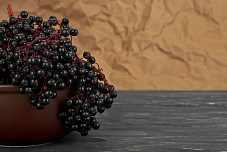 Berries of Elder Fruit in clay bowl, on wooden desk. Healing berries of ripe black elderberry.の写真素材