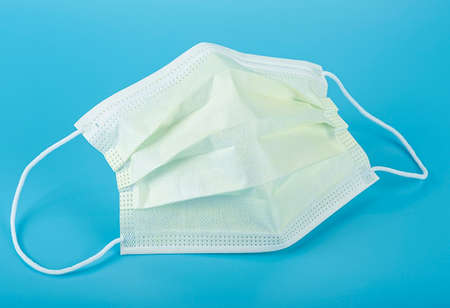 Yellow medical mask on blue background. Surgical mask with rubber ear straps.