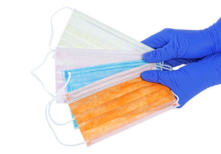 Hands in blue gloves holds a colorful medical face masks against viruses and bacteria on a white...