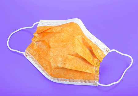 Orange medical mask on violet background. Surgical mask with rubber ear straps.の写真素材