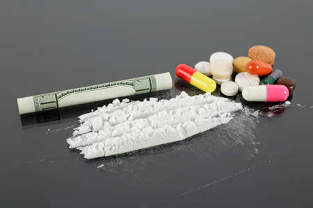Rolled hundred dollars banknote, cocaine powder and pile of pills on black background.の写真素材