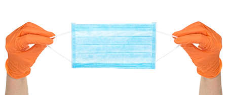 Hands in orange glove holds a blue medical face mask against viruses and bacteria on a white background. Protective medical tool.の写真素材
