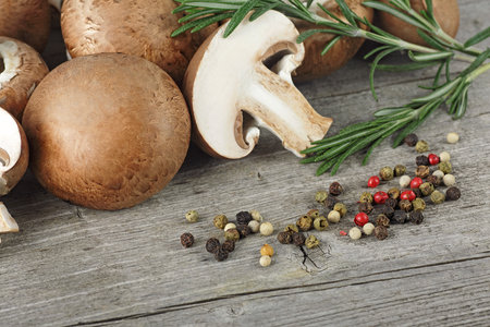 Fresh champignon mushrooms, rosemary and different peppercorns on wooden table.の写真素材
