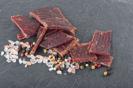 Beef jerky, peppercorns and sea salt on black stone table. Selective focus.の写真素材