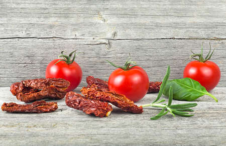 Traditional mediterranean kitchen - delicious dried tomatoes with fresh tomatoes, rosemary branch and basil leaf on wooden desk.の写真素材