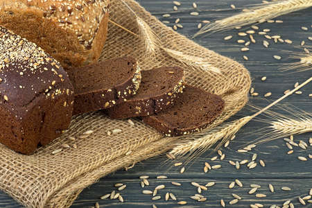 Freshly baked sourdough rye flour bread with flax and sesame seeds on wooden background. Ears of rye.の写真素材