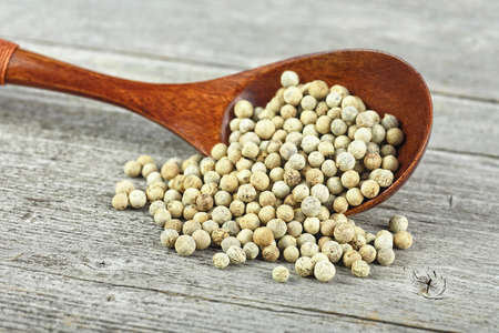 White pepper seeds in wooden spoon on rustic wooden table. White peppercorns.の写真素材