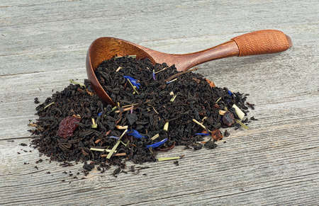 Black tea with dried fruits and petals in wooden spoon on a wooden table.の写真素材