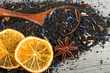 Black blended tea with flower petals and dried fruit in wooden spoon on a wooden desk. Black tea and dried oranges.の写真素材