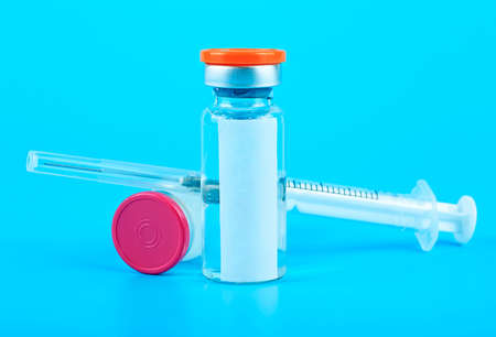 Glass vials with metal caps and injection syringe on blue background. Virus vaccine concept.の写真素材