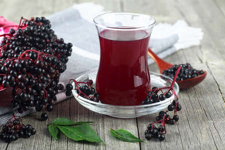 Elderberry syrup in a glass beaker with bunches of elderberries and elderberry leaves on wooden tableの写真素材