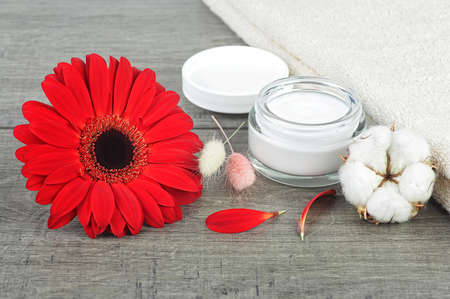 Face cream jar on wooden background with red gerbera, soft face towel and cotton flower.の写真素材