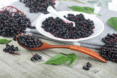 Delicious homemade black elderberry syrup and bunches of black elderberry with green leaves on...