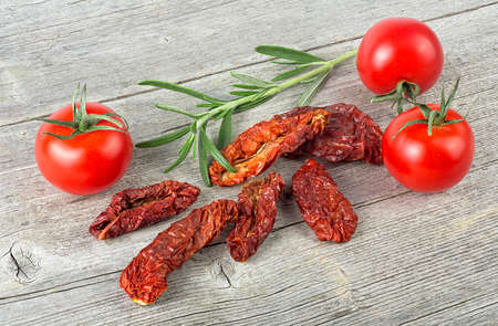 Traditional mediterranean kitchen - delicious dried tomatoes with fresh tomatoes and rosemary branch on wooden desk.の写真素材