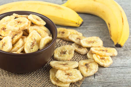 Healthy Food - Dried banana slices and fresh bananas on wooden table. Banana chips. Banana dessert.の写真素材