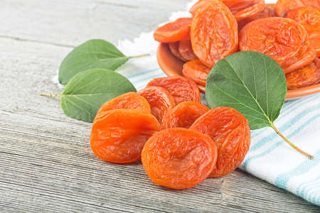 Delicious dried apricots in a bowl with green leaves on wooden deskの写真素材