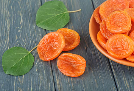 Dried apricots in bowl with green leaves on rustic wooden backgroundの写真素材