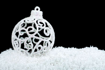 White decorative christmas ball on white snow on a black backgroundの写真素材