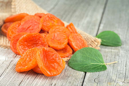 Dried apricots with green leaves on rustic wooden backgroundの写真素材