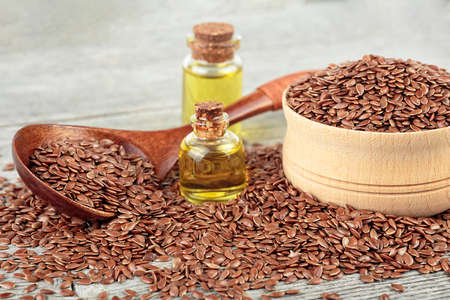 Linseeds in wooden spoon and flax oil in glass bottles on wooden table. Healthy food and drink concept.の写真素材