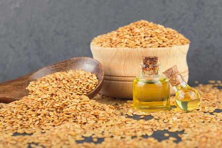 Linseeds in wooden spoon and flax oil in glass bottles on black stone table. Healthy food and drink concept.の写真素材
