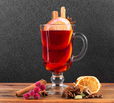 Cup of warm winter drink for christmas. Mulled wine with orange, anise, cardamom, nutmeg and cinnamon sticks on a brown table.の写真素材