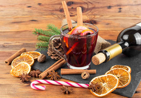 Delicious Christmas hot mulled wine, green pine tree branch, bottle of wine and spices on wooden background.の写真素材