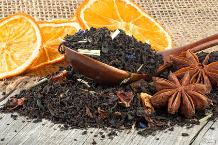 Black blended tea with flower petals and dried fruit in wooden spoon on a wooden desk. Black tea, anise stars and dried oranges.の写真素材