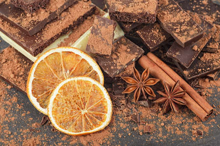 Broken chocolate pieces, cocoa powder, spices and dried oranges on a black backgroundの写真素材