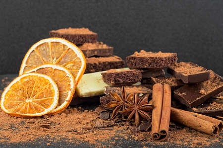 Broken chocolate pieces, cocoa powder, spices and dried oranges on a black backgroundの写真素材